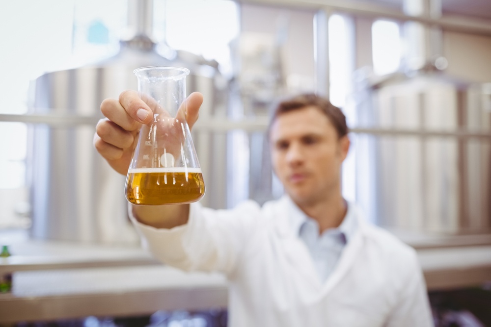Thoughtful scientist holding a beaker in the factory.jpeg